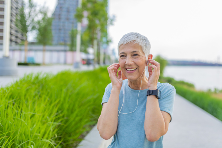 woman using hearing hearing aids while walking in the park and listening to music