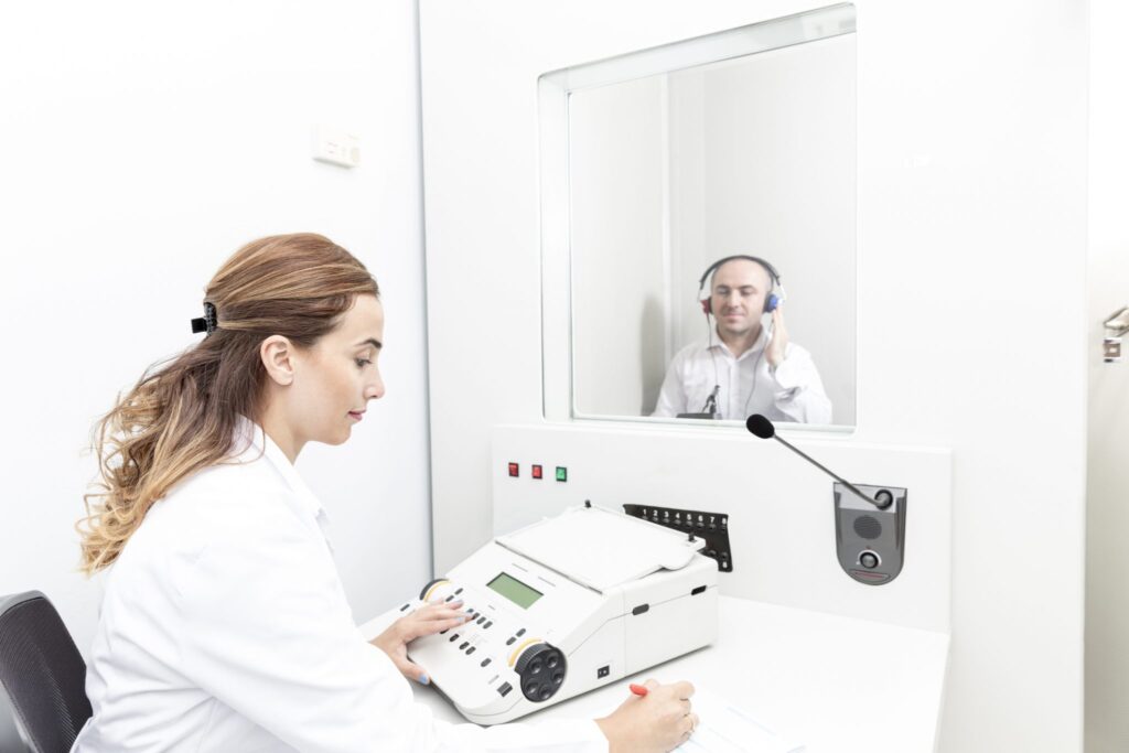 An audiologist performing a hearing test on a patient in a sound proof booth.