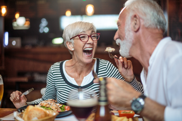 woman using her hearing aids in a restaurant laughing and enjoying conversation with her spouse