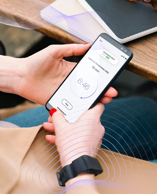 woman holding a cell phone that uses the Lenire tinnitus sound therapy device with a special wrist band